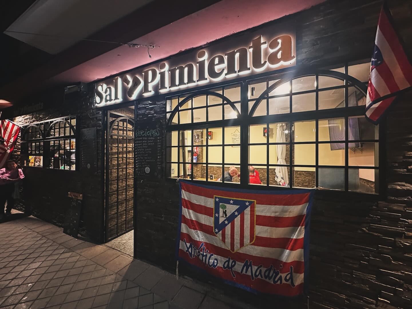Fachada de Sal y Pimienta Metropolitano de noche, con la bandera del Atleti en la ventana